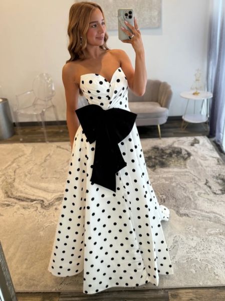 Front view of a playful polka dot strapless prom ball gown with a large oversized bow.
