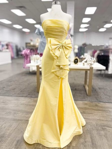 Yellow satin strapless mermaid prom dress with dramatic bow, high slit, and curve-hugging silhouette.